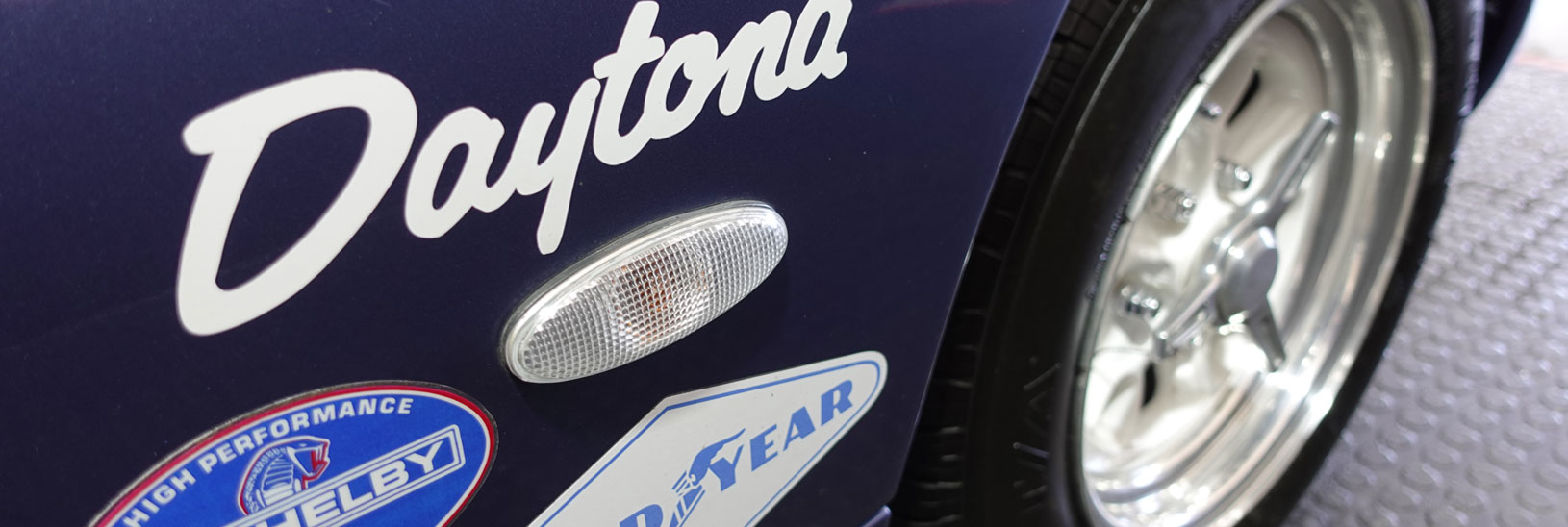 Close-up of purple Daytona coupe fender showing Daytona script, Shelby High Performance and Goodyear decals with polished alloy wheel